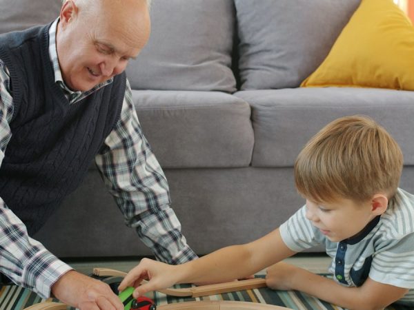 Happy boy is playing toy cars with loving grandad moving autos together smiling sitting on floor in apartment. Family relationship and lifestyle concept.