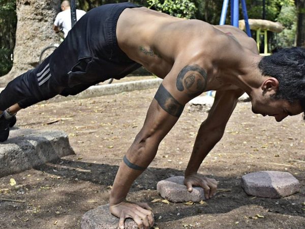 Athletic man performing elevated push-ups on rocks in a park setting.